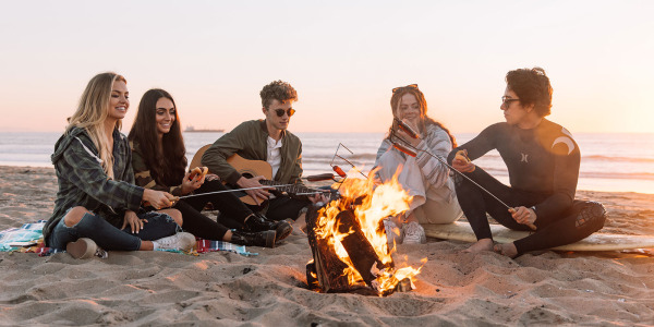 group of young people at the beach around a camp fire